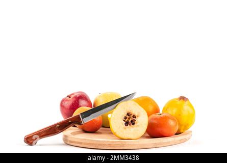 Mela cotogna tagliata a metà e frutta su un piatto di legno con fondo bianco a coltello. Frutti isolati. mandarino di mele mandarino e arancio su sfondo bianco Foto Stock