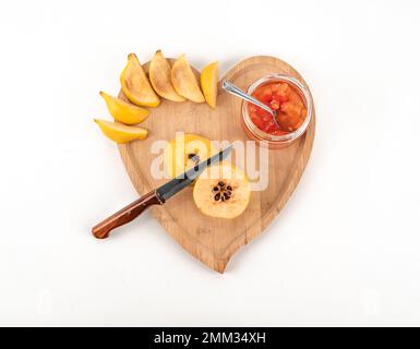 Vista dall'alto cucchiaio e coltello che tagliano fresca mela cotogna matura e marmellata su sfondo bianco isolato. Vetro chiaro maturo di vaso tutta la profondità di campo. cotogna fresca Foto Stock