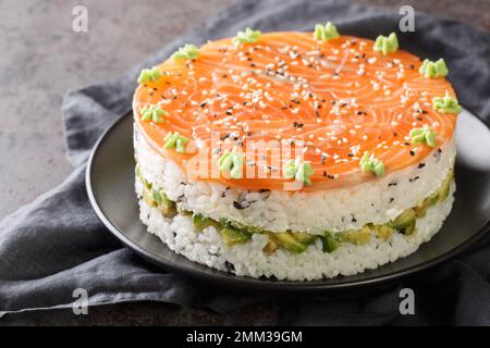 Torta di sushi con salmone, riso, avocado e Philadelphia primo piano sul piatto sul tavolo. Orizzontale Foto Stock