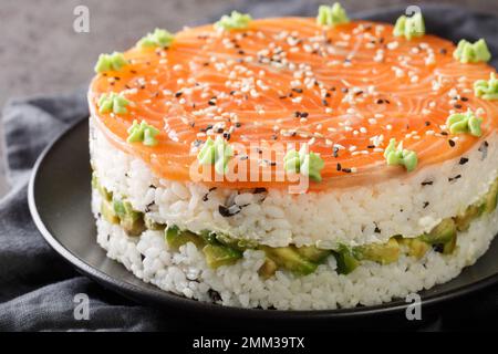Deliziosa torta di sushi philadelphia con pesce rosso, riso, avocado, formaggio spalmabile, alghe, semi di sesamo decorati con wasabi close-up in un piatto sulla t Foto Stock