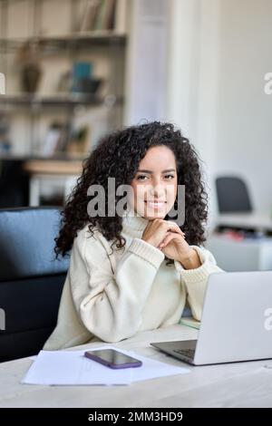 Giovane donna business latino felice seduta alla scrivania dell'ufficio con un computer portatile. Verticale Foto Stock
