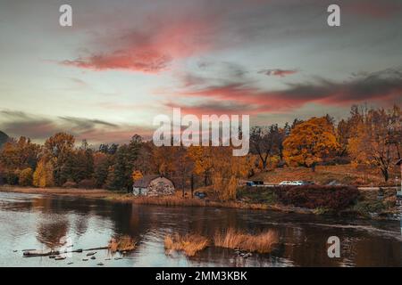 Vecchia casa nel mezzo di una foresta in autunno vicino al fiume con cielo rossiccio e alberi gialli Foto Stock