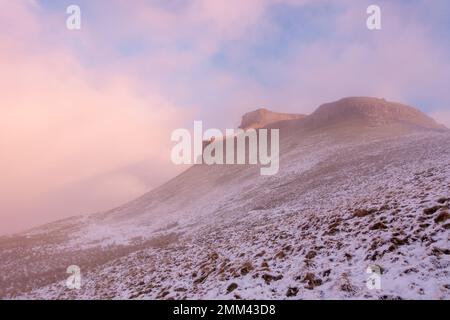 Guardando verso la cima del monte Pen-y-ghent all'alba nella neve d'inverno, la nebbia si chiarisce e la luce cattura la cima rocciosa dello Yorkshi Foto Stock