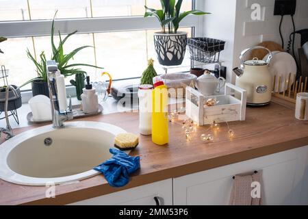 Pulizia della cucina prima delle vacanze di Natale e Capodanno. Detersivo, polvere secca, spugna, guanti sono sul lavello. Decorazioni natalizie nella divisa bianca Foto Stock