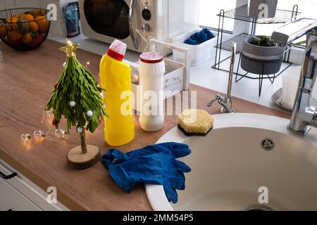 Pulizia della cucina prima delle vacanze di Natale e Capodanno. Detersivo, polvere secca, spugna, guanti sono sul lavello. Decorazioni natalizie nella divisa bianca Foto Stock