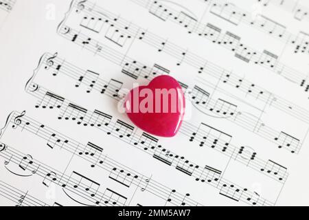 Vista dall'alto del piccolo cuore rosso su foglio di carta con note musicali da vicino. Foto Stock