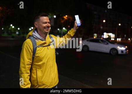 Giovane uomo bello con zaino e smartphone in mano incontra gli amici o taxi sulla strada cittadina. Foto Stock
