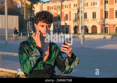 Il giovane uomo indossa il make-up mentre si guarda al telefono Foto Stock