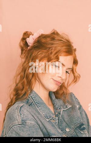 Ritratto di donna sorridente in giacca denim con crunchie rosa Foto Stock