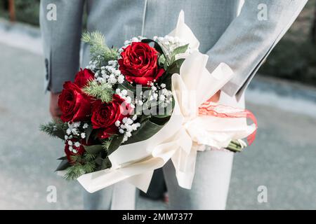Primo piano di un uomo con bouquet di rose dietro la schiena. San Valentino Foto Stock