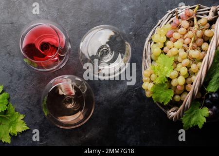 Bicchieri da vino bianco, rosato e rosso e uva in cesto. Giacitura piatta Foto Stock