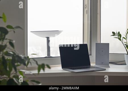 KIEV, UCRAINA - 24 GENNAIO 2023: Antenna Starlink dietro la finestra con router wi-fi e laptop sul davanzale in casa. Foto Stock