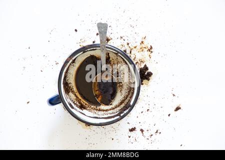 una tazza con caffè capovolto su sfondo bianco e un cucchiaino da tè si trova accanto ad esso, caffè versato su sfondo bianco Foto Stock