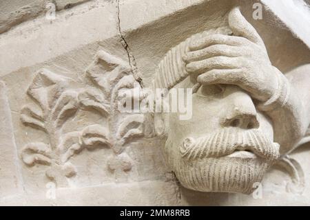 Testa grottesca in pietra scolpita di un uomo apparentemente affetto da mal di testa, su una colonna del 12th ° secolo nella Chiesa di San Giovanni Battista, Bere Regis, Dorset. Foto Stock