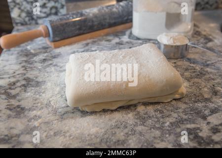 Pasta sfoglia fatta in casa con farina e un matterello sul piano della cucina in marmo Foto Stock