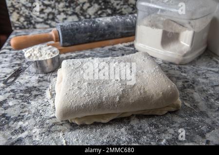 Pasta sfoglia fatta in casa con farina e un matterello sul piano della cucina in marmo Foto Stock