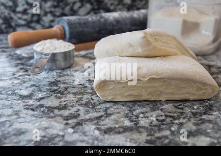 Pasta sfoglia fatta in casa con farina e un matterello sul piano della cucina in marmo Foto Stock