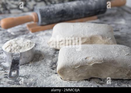 Pasta sfoglia fatta in casa con farina e un matterello sul piano della cucina in marmo Foto Stock