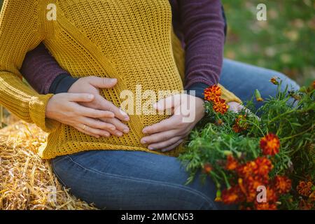 Un uomo abbraccia il ventre di una donna incinta. Gravidanza, amore, famiglia e concetto di persone - primo piano di donna incinta facendo mano cuore gesto sul suo ventre. Foto Stock