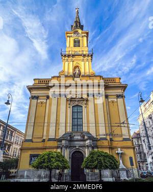 La cattedrale di Santa Teresa si trova all'angolo della strada nel centro storico di Budapest, in Ungheria. Le belle nuvole blu del cielo delineano il campanile e la croce. Foto Stock