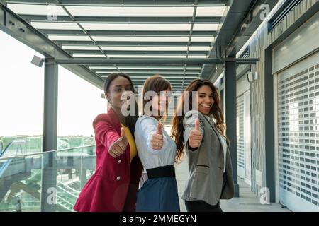 Tre giovani donne d'affari con i pollici in su per il successo di affari. Sembrano molto felici Foto Stock