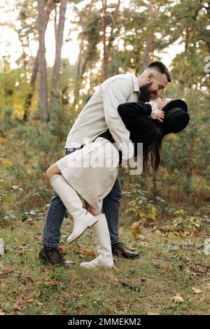 Felice giovane uomo bearded con la sua ragazza sono abbracciato nel parco nel caldo giorno di San Valentino. Amorevole coppia eterosessuale alla moda che si diverte e guarda Foto Stock