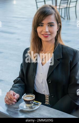 Una giovane donna d'affari prende una pausa caffè; sorride alla macchina fotografica. Immagine verticale Foto Stock
