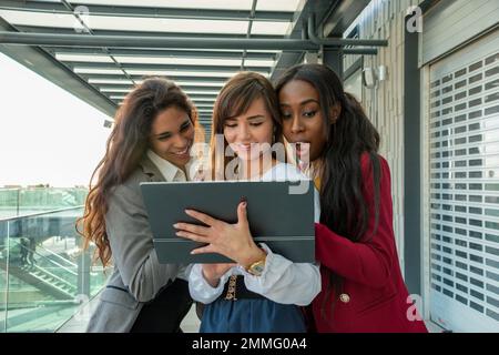 Tre giovani imprenditrici che consultano i progressi aziendali sul loro tablet sono rimasti positivamente sorpresi Foto Stock