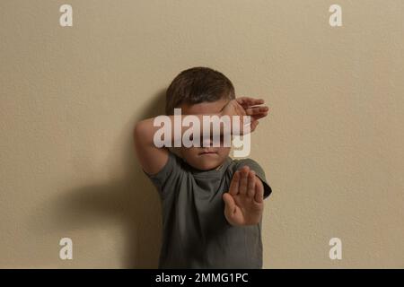 Piccolo ragazzo spaventato che chiude il volto con la mano su sfondo giallo. Bambini in pericolo Foto Stock