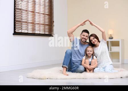 Famiglia felice che forma il tetto della casa con le loro mani a casa. Concetto di assicurazione Foto Stock