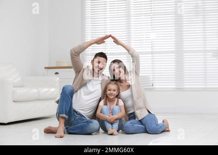 Famiglia felice che forma il tetto della casa con le loro mani a casa. Concetto di assicurazione Foto Stock