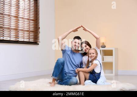 Famiglia felice che forma il tetto della casa con le loro mani a casa. Concetto di assicurazione Foto Stock