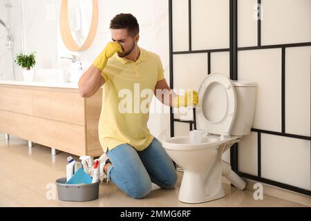 Giovane uomo che sente disgusto mentre pulisce il water ciotola in bagno Foto Stock