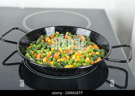 Cucinare gustoso impasto di verdure surgelate su stufa a induzione Foto Stock