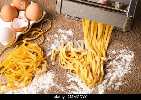 Macchina per pasta con pasta e prodotti su tavolo di legno, piatto Foto Stock