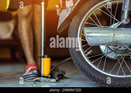 Un giovane uomo controlla la pressione del generatore di gas e gonfia lo pneumatico sulla motocicletta con la pompa da pavimento per bicicletta. Persone che controllano la pressione dell'aria e che riempiono la pressione dei pneumatici Foto Stock