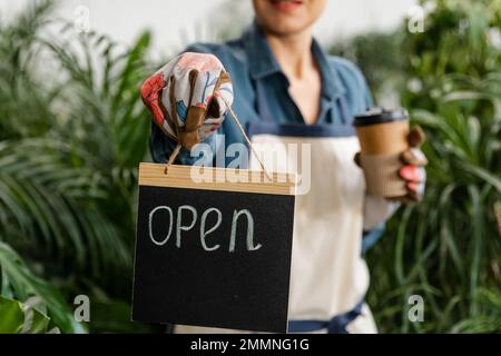 Imprenditore femmina in possesso di aprire segno in mani in negozio floreale. Foto Stock