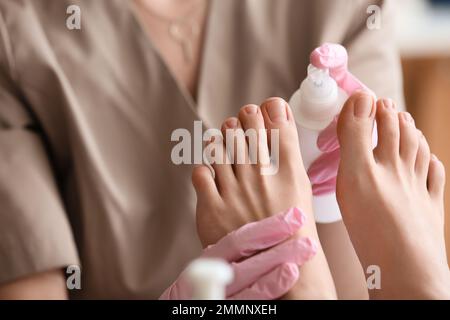 Estetista spruzzando prodotto cosmetico sui piedi della donna in salone, primo piano Foto Stock