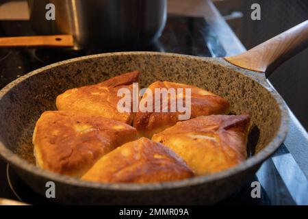 Friggete deliziose torte fatte in casa con carne ripieno di olio vegetale caldo. Le torte vengono fritte in una padella. Cucina russa. Foto Stock