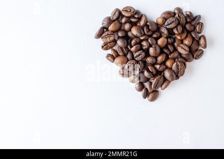 Simbolo dell'amore per il caffè. Forma del cuore in chicchi di caffè su sfondo bianco, primo piano, vista dall'alto, disposizione piatta, spazio copia, banner Foto Stock