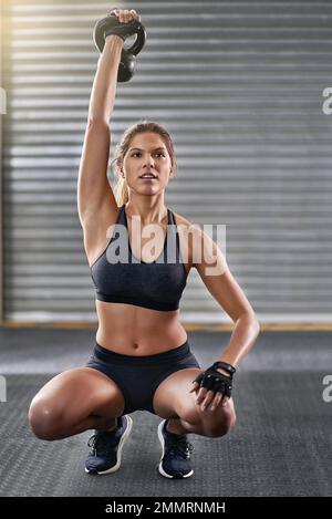 I suoi obiettivi di fitness sono a portata di mano. Foto a tutta lunghezza di una giovane donna che si allenava con una campana del bollitore in palestra. Foto Stock