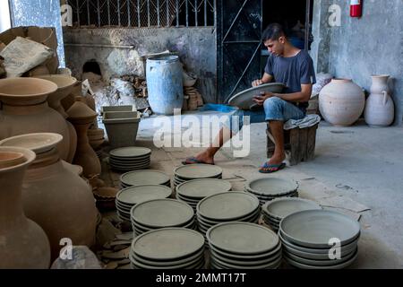 Un lavoratore siede su una cassa di legno mentre leviga ciotole di ceramica in una fabbrica a Fez in Marocco. Foto Stock