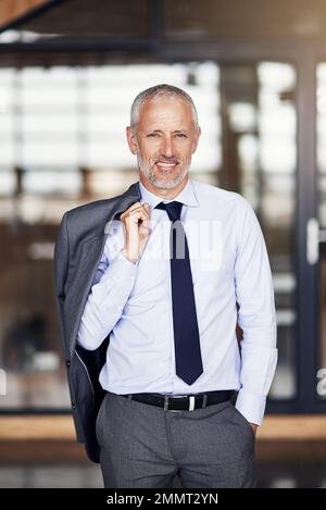 HES un uomo d'affari molto rispettato. Ritratto corto di un uomo d'affari maturo in piedi con il suo blazer sfilato sopra la sua spalla. Foto Stock
