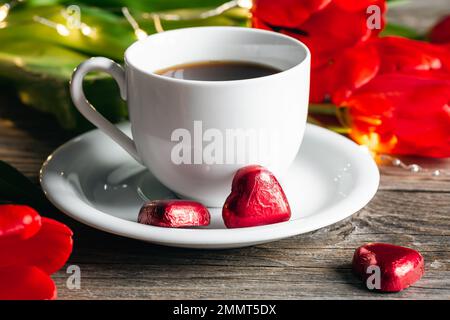 Composizione con una tazza di caffè, dolci a forma di cuore e fiori rossi in primo piano. Foto Stock