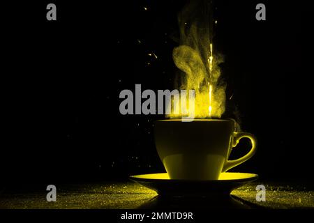 Una tazza con una bevanda calda e vapore illuminato da luce gialla, spazio copia, creativo. Tazza da caffè fumante su sfondo nero, silhouette. Mattina co Foto Stock