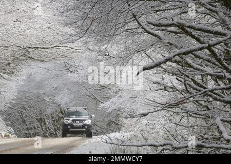 Un'auto viaggia attraverso la panoramica azienda vinicola Exmoor dopo una nevicata che attraversa la Gran Bretagna, Regno Unito Foto Stock