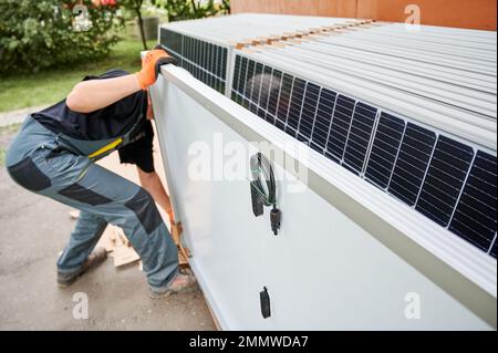 Lavoratore che prende pannello solare per il trasporto e l'installazione. Energia rinnovabile ed ecologica. Idea di ambiente sicuro. Tecnologia moderna e innovazione. Uomo che indossa indumenti da lavoro e guanti da lavoro Foto Stock