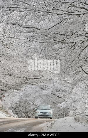 Un'auto viaggia attraverso la panoramica azienda vinicola Exmoor dopo una nevicata che attraversa la Gran Bretagna, Regno Unito Foto Stock