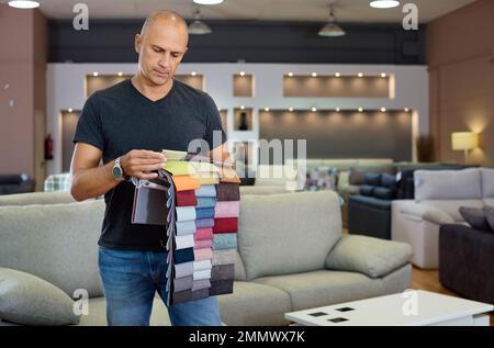 Ritratto dell'uomo che tiene e sceglie campioni di tessuto di tappezzeria in salone di mobili Foto Stock