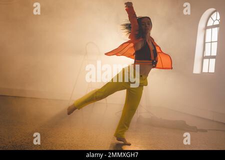 Immagine di danza moderna femminile biraciale in interni affumicati. Danza, arte del ritmo e concetto di movimento. Foto Stock